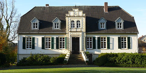 Ansicht des Haupthauses auf Haus Darup: weißes herrschaftlich wirkendes Haus mit zentraler Freitreppe und grünen Fensterläden.