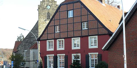 Seitenansicht der Alten Diele. Rot getünchte Mauern, weiße Fensterrahmen und im Obergeschoss ist das Fachwerk zu sehen.
