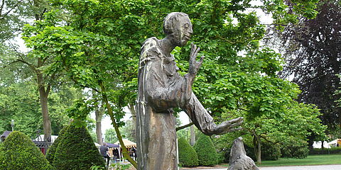 Bronzeskulptur des heiligen Franziskus, der sich segnend und mit freundlichem Gesicht einem Wolf zuwendet.f 