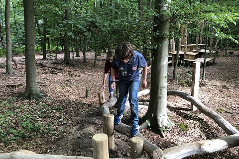 Oma und Enkel balancieren gemeinsam im Walderlebnisraum.