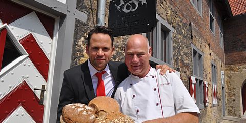 WDR-Moderator Christoph Tiemann und der Inhaber des Cafés Reitstall, Jörg Terjung, halten frisch gebackenes Brot zur Kamera. 