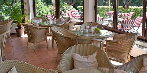 Helles Ambiente im Café mit Korbstühlen und Blick durch die großen Scheiben auf die Außenterrasse